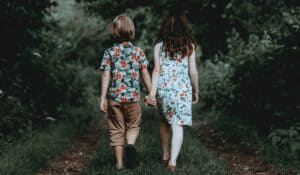 two children holding hands walking away down a grassy dirt path