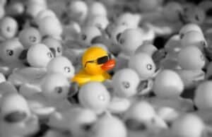 a yellow rubber duck standing out in a crowd of grayscale rubber ducks